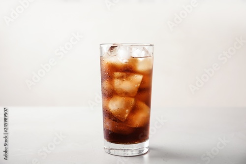 Glass of refreshing cola with ice on white table