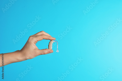 Female doctor holding hearing aid on color background, closeup view with space for text. Medical object