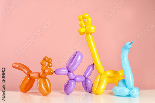 Animal figures made of modelling balloons on table against color background