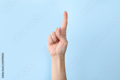 Woman showing number one on color background, closeup. Sign language photo
