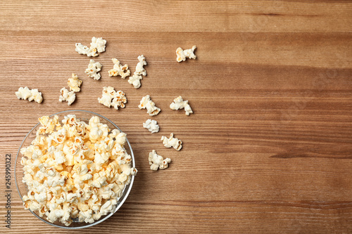 Glass bowl with tasty popcorn on wooden background, top view. Space for text