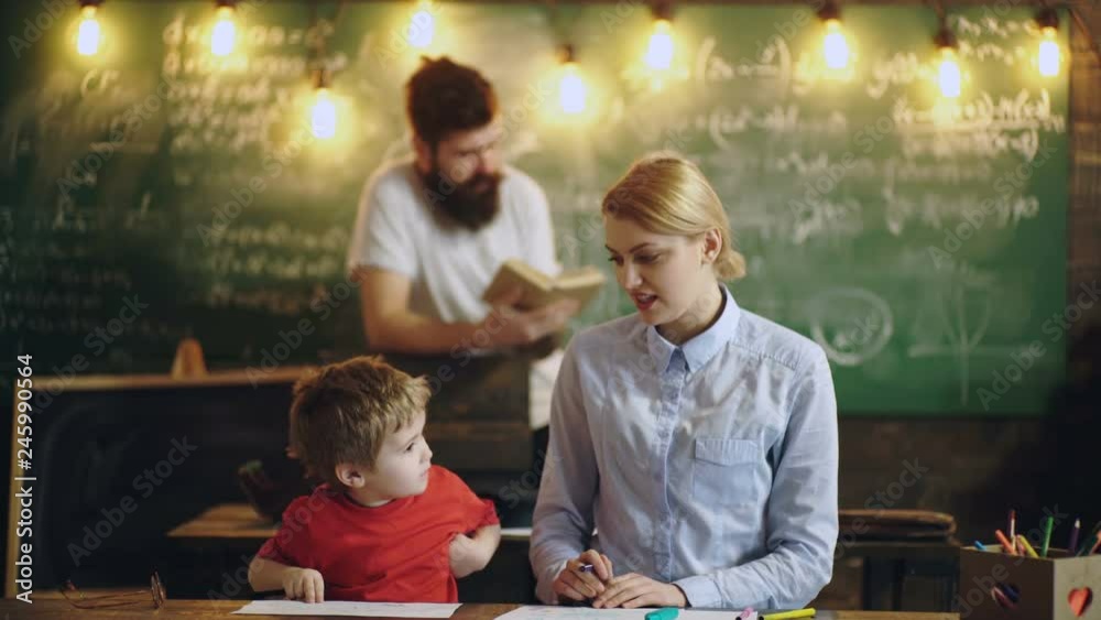 Teacher and little boy draw and talk on the background of a green board and bearded professor. Back to school background with books and profesor over blackboard. Learning concept.