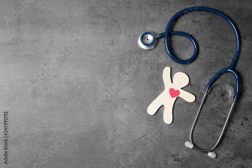 Stethoscope with human figure and heart on grey background, flat lay. Space for text