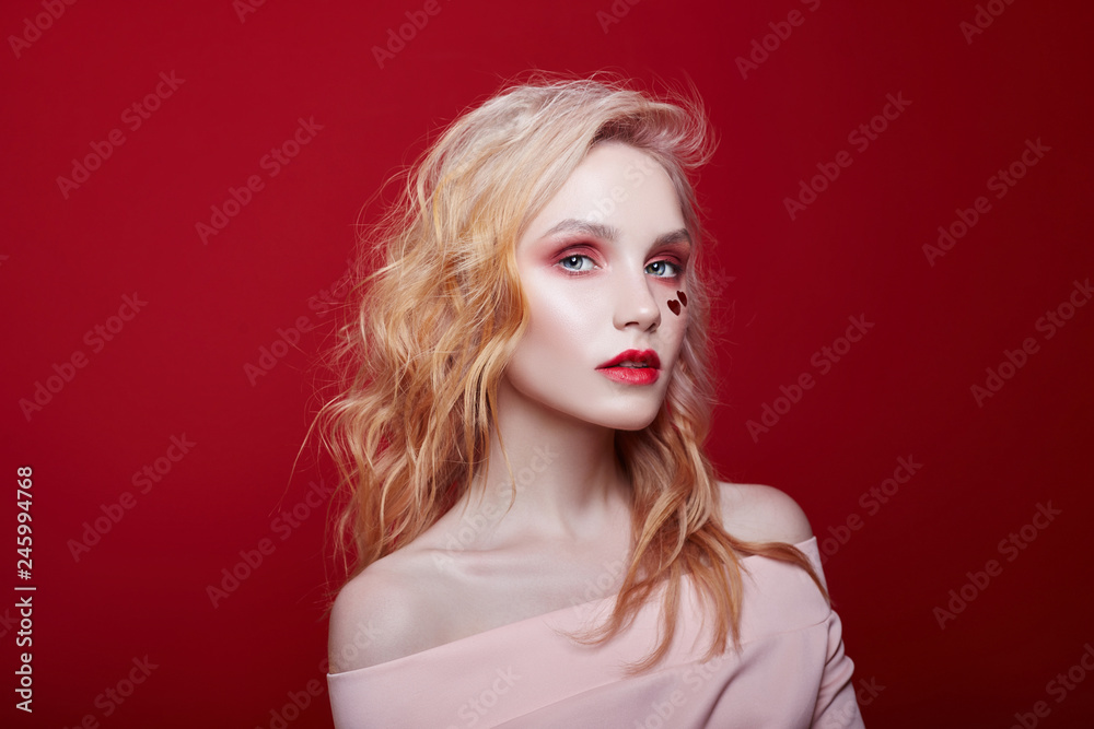 Slender blonde girl, perfect figure and long hair. Clean perfect face skin. Portrait of sexy fashion beautiful blonde woman with bright makeup posing on red crimson background