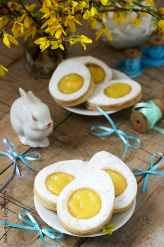 Easter composition with egg-shaped cookies filled with lemon curd, rabbit, bouquet of forsythia and bows. photo