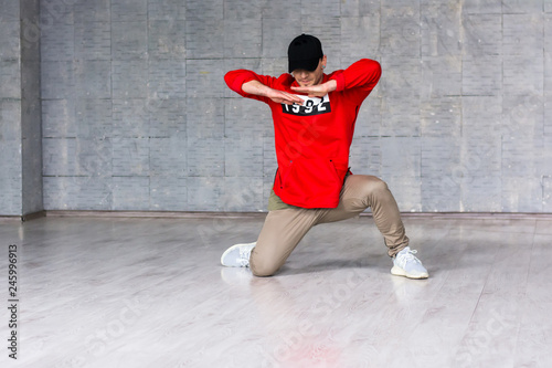 Young dancer posing on grey floor. Stylish hip-hop dancer making movement with hands on grey background.