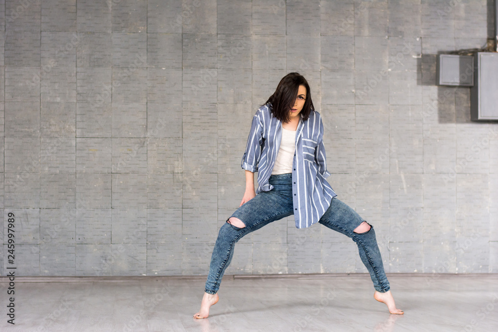 Modern style girl posing on grey background. Young pretty dancer woman performing dance element on studio background. Modern style girl posing on grey background. Young pretty dancer woman performing dance element on studio background.