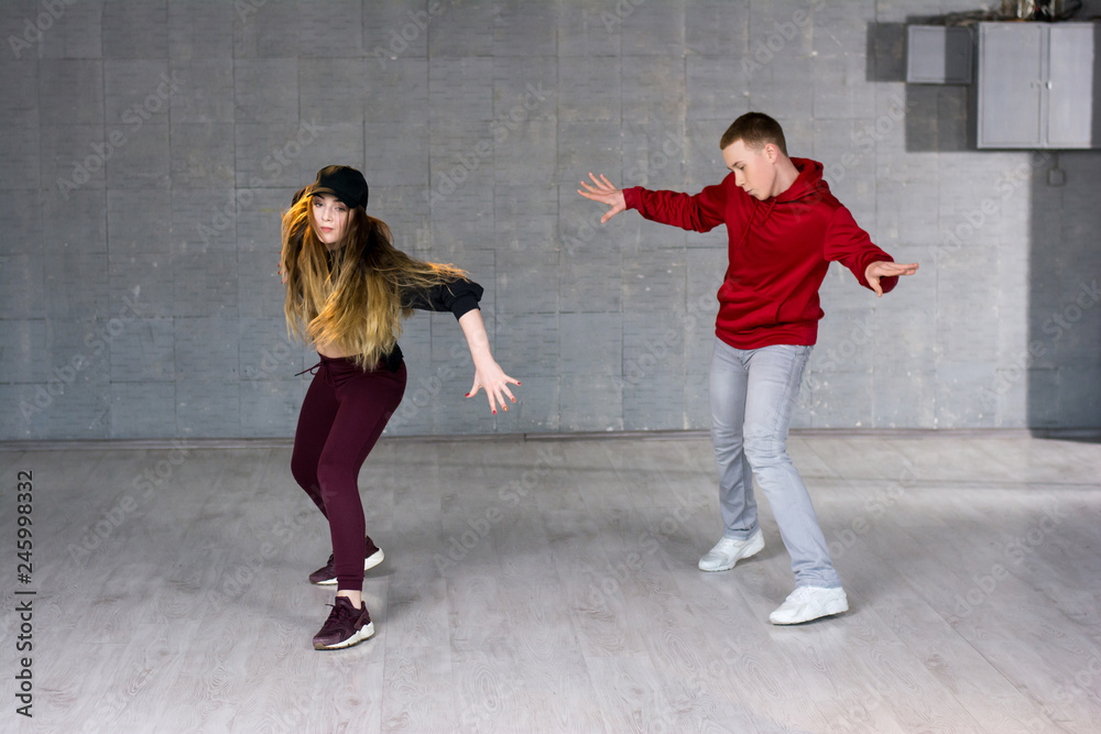 Attractive casual couple dancing hip-hop. Two modern style beautiful performers working out on studio background.