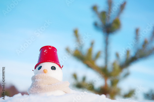 Little snowman with a bucket on the head and in a scarf on snow in sunny winter day