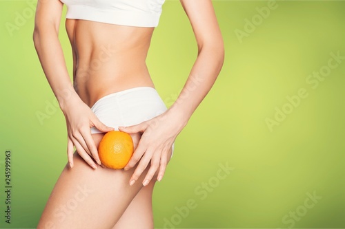 Female slender body in sport underwear holding orange on white