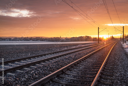 Railway tracks through frozen nature at sunrise. Traveling context. Winter holiday travel.