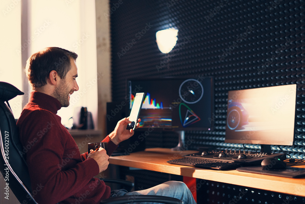 Young man working in the studio using a smartphone and computer. Young man working in the studio using a smartphone and computer.