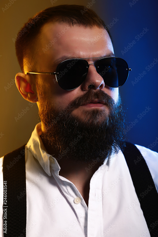 Obraz premium young handsome man with big beard and black sunglasses on black background 