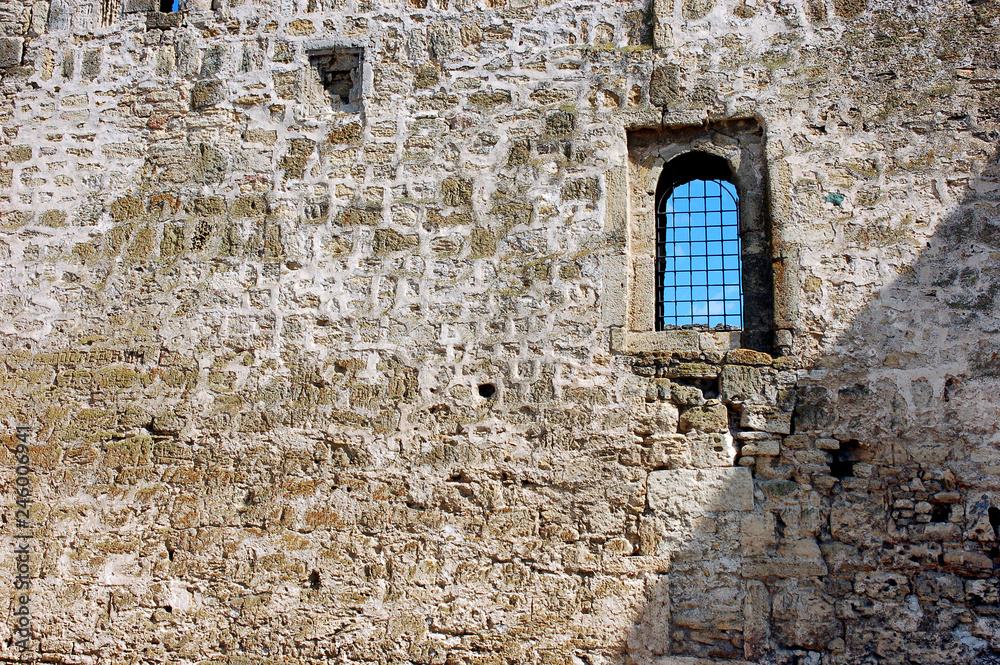 Old stone wall built of limestone bricks with a small window wi Old stone wall built of limestone bricks with a small window wi
