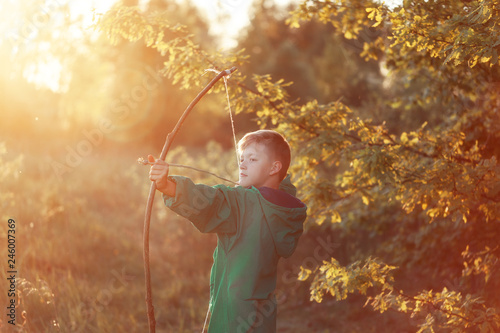 Young boy, shoot with handmade bow and arrow at target on sunset, summertime outdoors.