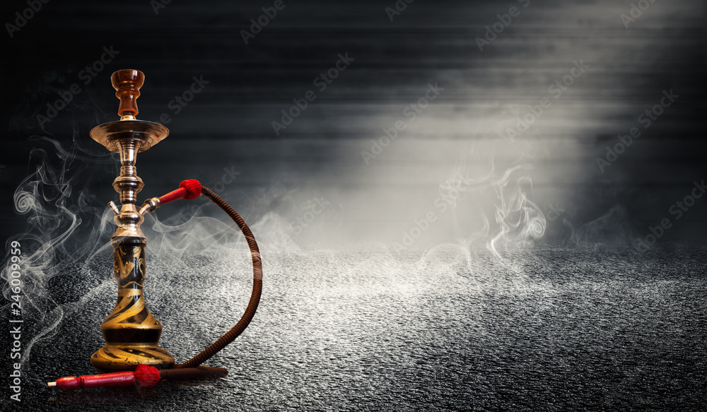 Smoking hookah on the background of an empty wooden wall and concrete floor. Spotlight, neon light, smoke