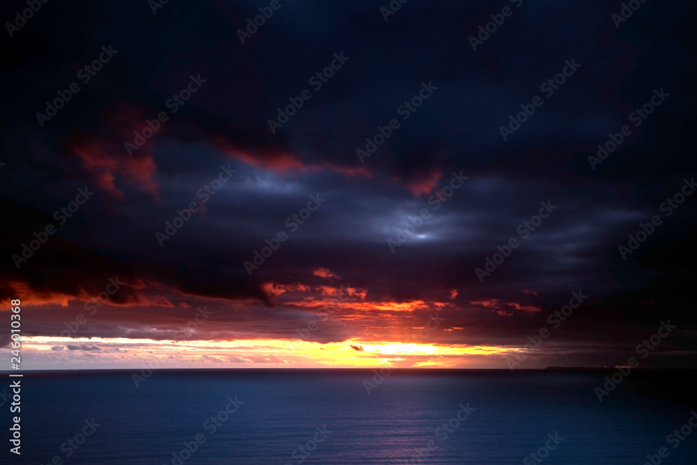 Inspirational, blazing, striking red sunset over the ocean. Blurry, moving sky, horizon in focus.