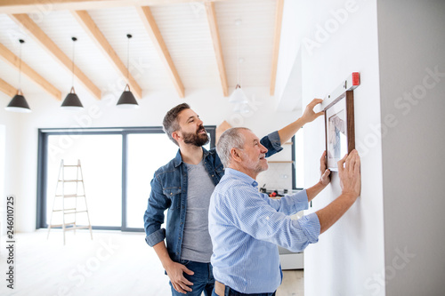 Tableau sur toile A senior man helping his son hanging up pictures on wall, a new home concept
