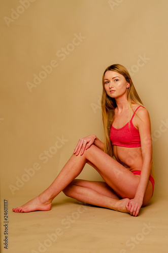 model blonde in red in the studio on a homogeneous beige background of a bodily color. Sexy girl in swimsuit