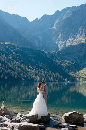 Beautiful wedding couple in love standing on the stony shore of the Morskie Oko lake in Poland. Scenic mountain view