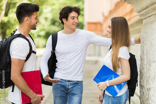 Tablou pe pânză Three students talking to each other outdoor in a college courtyard