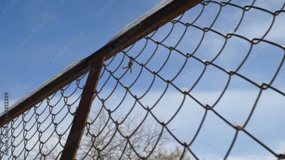 Chain link fence against sky in winter. Snow melting on metal wires of chain-link fencing. Gimbal steadicam movement. Chain link fence against sky in winter. Snow melting on metal wires of chain-link fencing. Gimbal steadicam movement.