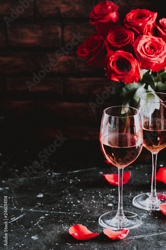 Two wine glasses of rose wine on brick background, bouquet of red roses for romantic evening for Valentines day surprise, marriage proposal passion and love celebration, copy space 