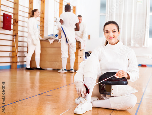 Woman in uniform sitting on floor at fencing training