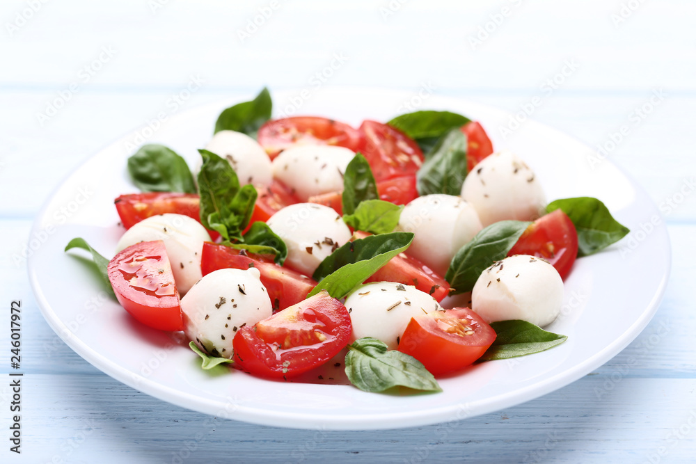Mozzarella, tomatoes and basil leafs in plate on wooden table Mozzarella, tomatoes and basil leafs in plate on wooden table