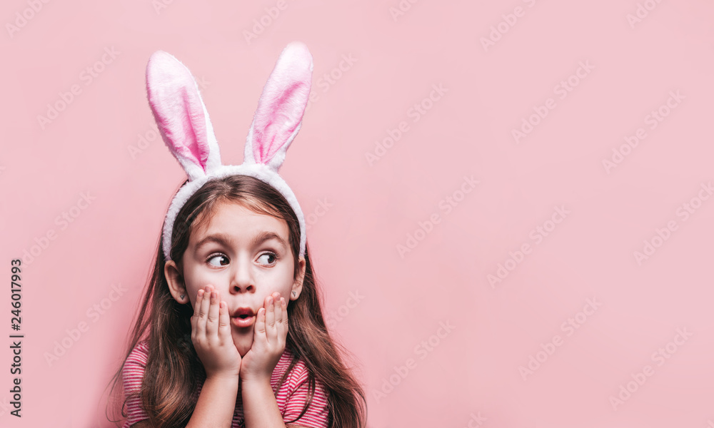 Cute little Cute little girl with bunny ears on pink background. Easter child portrait, funny emotions, surprise. Copyspace for text.with bunny ears on pink background.