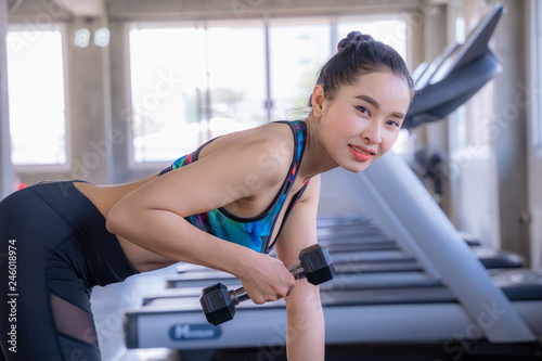 Asian beautiful woman is lifting double in the gym, She smile happily in exercise because it makes her shapely, the concept of exercise, lose weight, strengthen muscles.
