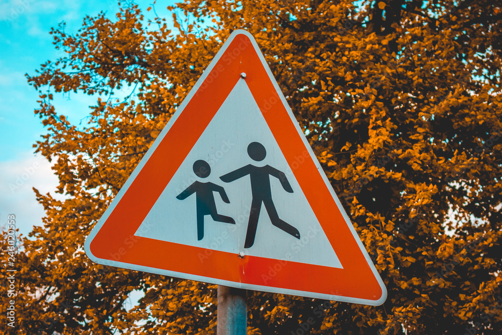 red triangle pedestrians traffic sign with orange tree in the background red triangle pedestrians traffic sign with orange tree in the background