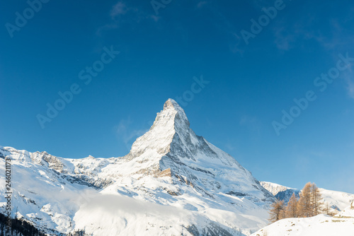 Scenery view on snowy Matterhorn peak in sunny day with blue clear sky and some clouds and other mountains, Switzerland