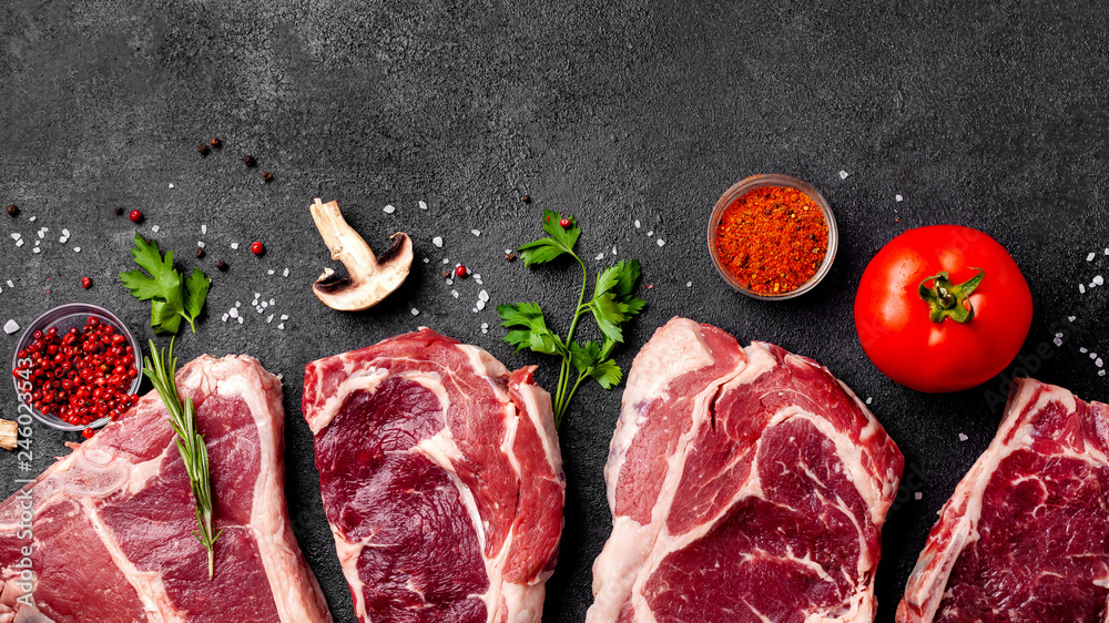 Meat raw steaks lie on a black background with vegetables, tomatoes, marasmade, mushrooms. background image. side view, copy space, top view