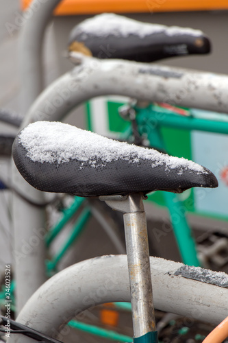 Snowy saddles of bicycles stand on a winter street.