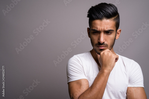 Young handsome Persian man against gray background