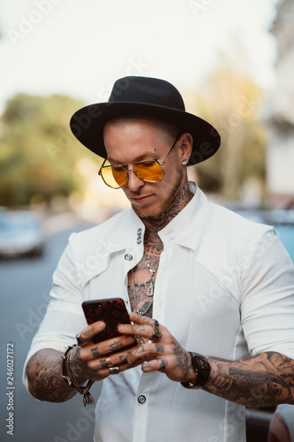 A young man in a hat and sunglasses holds a mobile phone in his hands