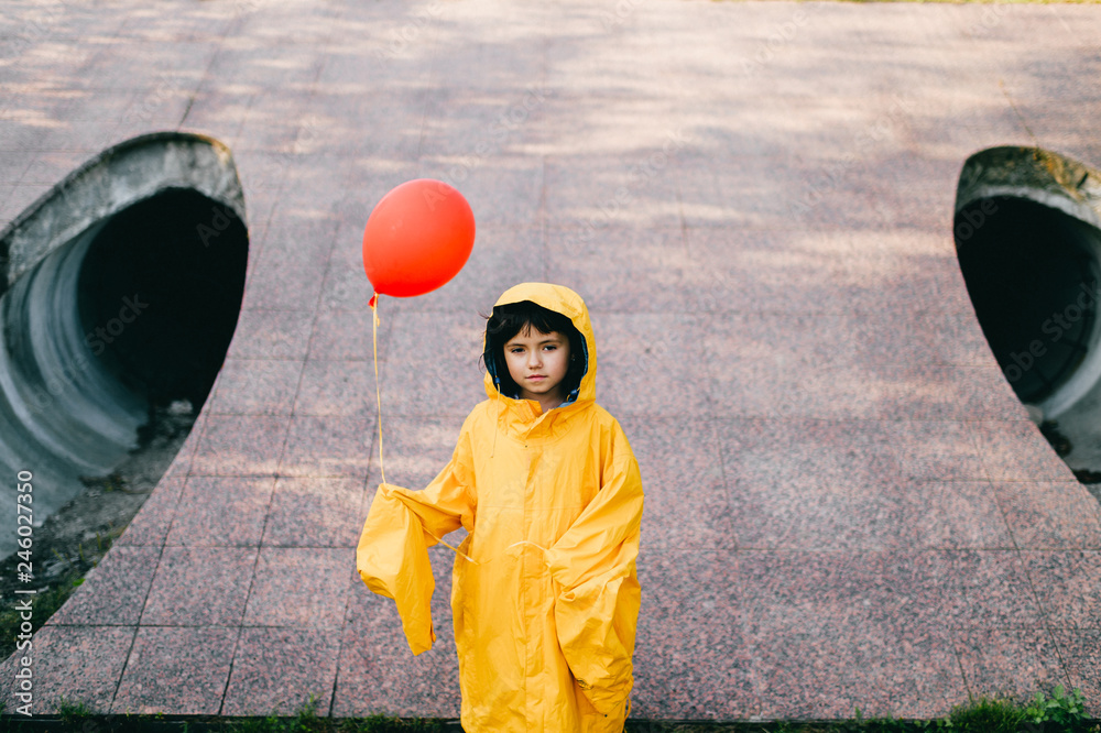Portrait of pretty litle girl in big adult oversized yellow raincoat with red  balloon in hand