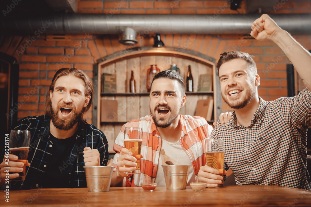 Sports fans funny friends men sit in bar drink beer and watch football match on TV in pub
