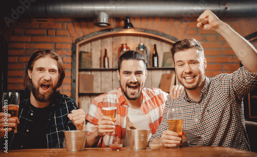 Cheerful friends men fans watch sports match on TV and drink draft beer in bar pub photo