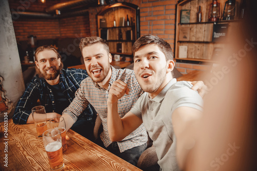 Cheerful friends make selfie photos and drink draft beer at pub bar. Friendship concept