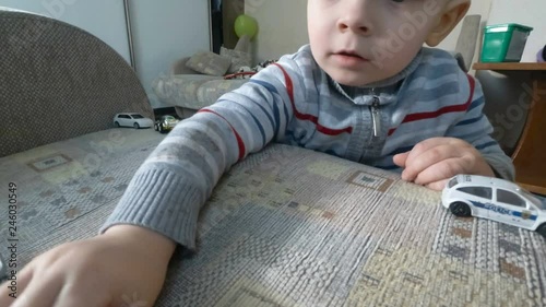 A little baby boy playing with his toys on armchair. Toddler boy is playing with toy cars.