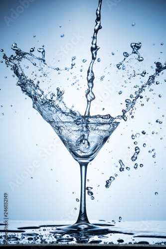 Splashing water on blue background. Cocktail glass with water.