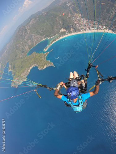 Paragliding in the sky. Paraglider tandem flying over the sea with blue water and mountains in bright sunny day. Aerial view of paraglider and Blue Lagoon in Oludeniz, Turkey. Extreme sport. Landscape