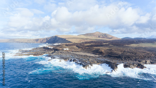 Aerial view of a fishing village on a rocky shore battered by high sea waves, with volcanic mountains on horizon, , Lanzarote, Canary Islands, Spain .