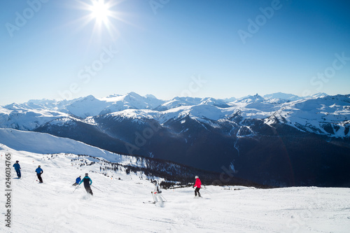 Skiers on a hill at the top of Blackcomb, 7th Heaven, with a view looking toward Whistler on a sunny day.