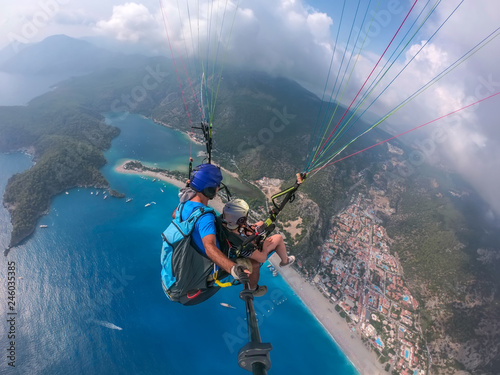 Paragliding in the sky. Paraglider tandem flying over the sea with blue water and mountains in bright sunny day. Aerial view of paraglider and Blue Lagoon in Oludeniz, Turkey. Extreme sport. Landscape