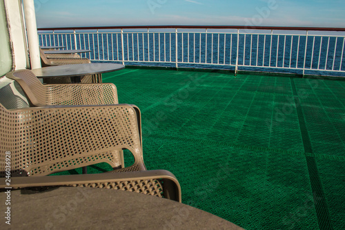 food terrace in a boat with brown plastic chairs and tables  a green plastic floor  railing and the view from the ship to the atlantic ocean 