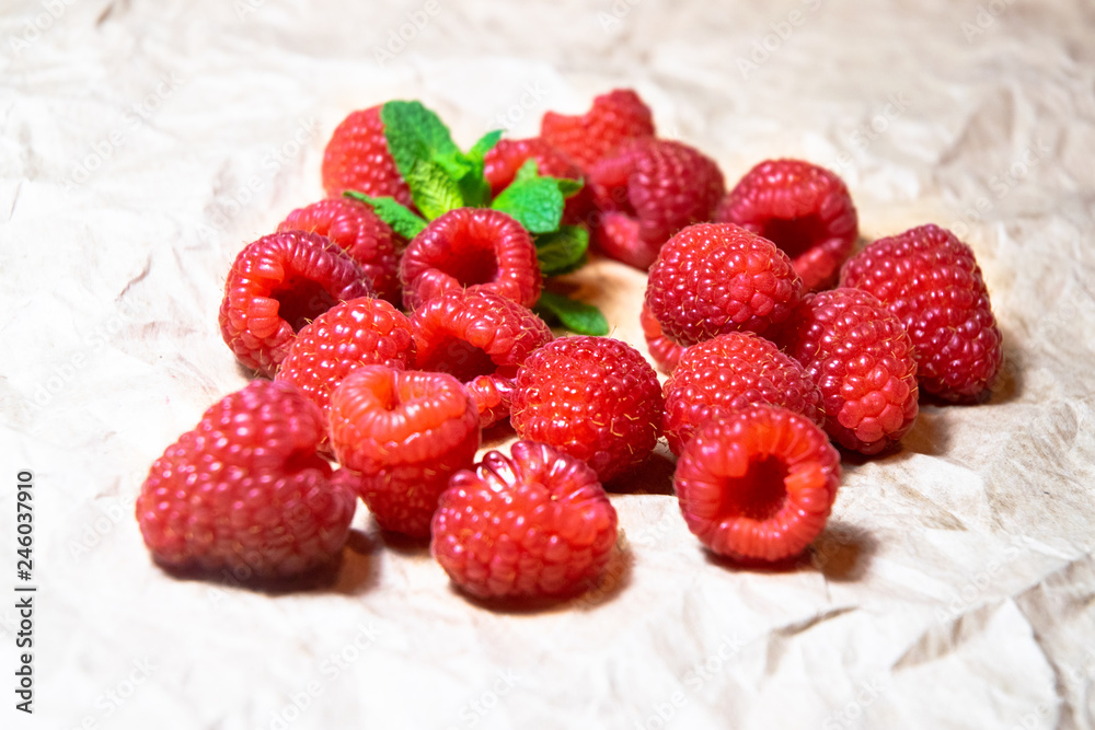 A small pile of juicy delicious red raspberries decorated with fresh mint on the plain bright paper background A small pile of juicy delicious red raspberries decorated with fresh mint on the plain bright paper background