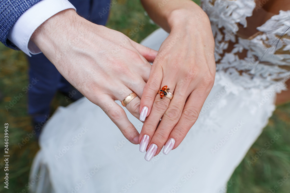 Naklejka premium ręce są świeżo poślubione ze złotymi obrączkami. dwie złote obrączki ślubne na palcach narzeczonych czerwony chrząszcz na dłoni młodej kobiety